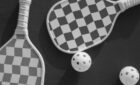 Checkered pickleball paddles and balls on a dark background, viewed from above.